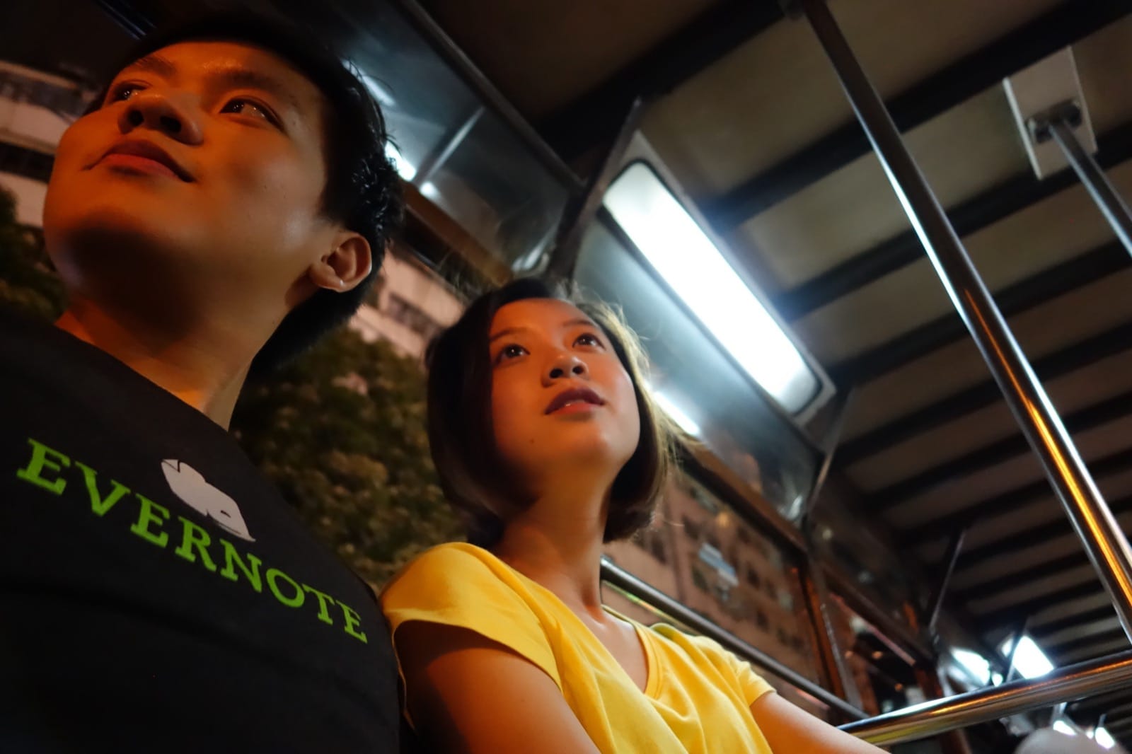Flora and Hanny on a Hong Kong tram at night, city lights behind them.