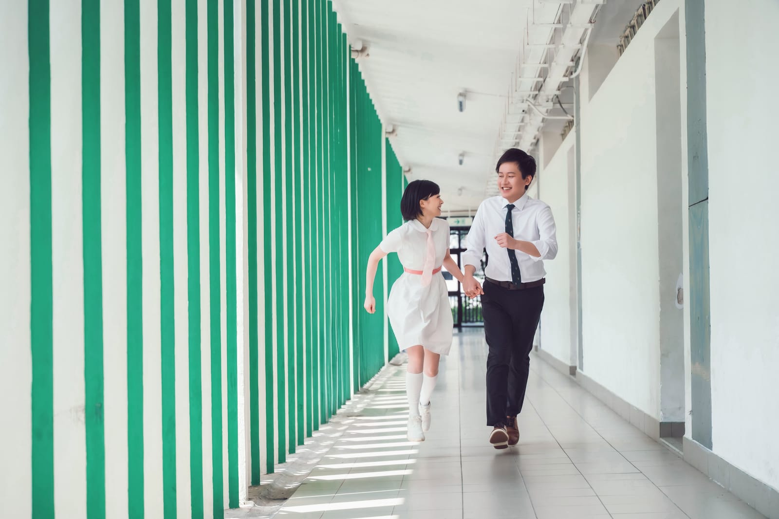 Flora and Hanny running hand in hand down a green-and-white striped corridor, laughing.