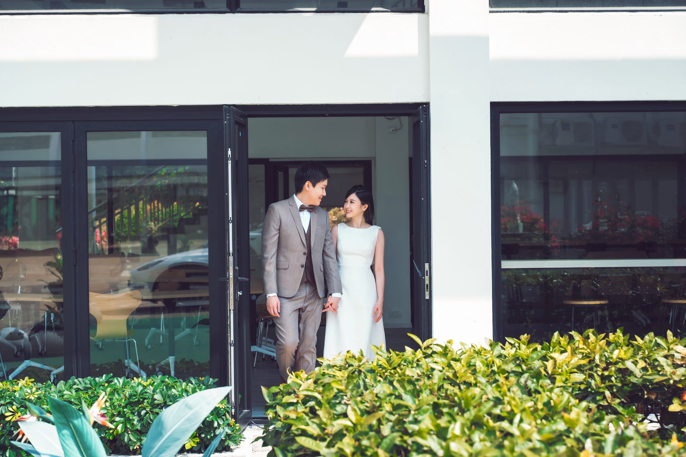 Flora and Hanny in wedding attire, stepping out into a garden.
